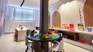 A children's play area with a tree-shaped play structure, a round table with chairs, and educational toys on shelves. - Lindo Estúdio com Jacuzzi, Sauna e Coworking (Maceió)