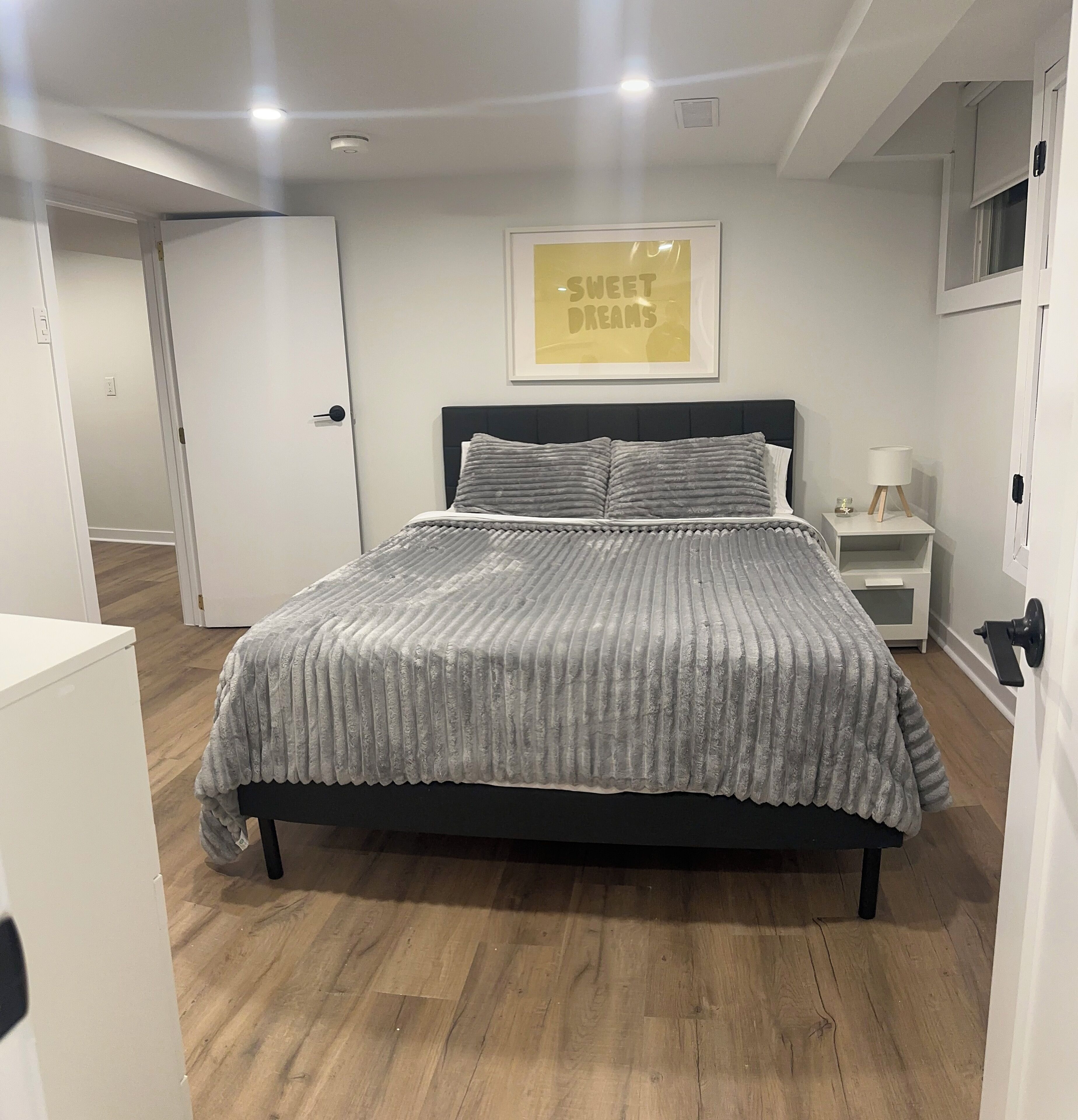 A neatly arranged bedroom with a bed, a bedside table, a nightstand, and a framed picture on the wall.