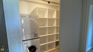Une buanderie équipée d’un lave-linge et d’un sèche-linge, avec un plancher en bois et une étagère blanche.