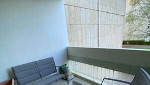 Un balcon avec un canapé gris, une petite table et une chaise. On y trouve une plante en pot et un paquet de chips sur la table.