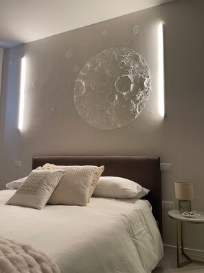 A bedroom with a bed, pillows, a bedside table with a lamp, and a wall-mounted light fixture.