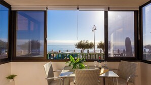 Un comedor con mesa y sillas, una planta en maceta y vista al mar a través de amplias ventanas.