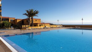 Una piscina con sillas de descanso y una palmera, rodeada de edificios bajo un cielo despejado.
