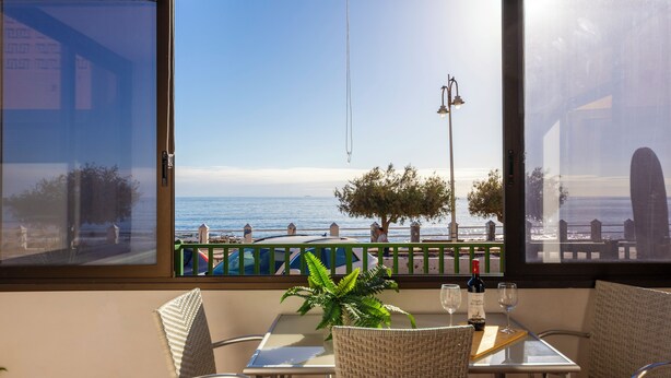 Una mesa con sillas y una planta en maceta, con vista a una playa que tiene una barandilla y un farol.