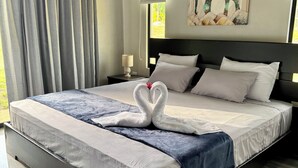 A hotel room with a large bed, a headboard, a nightstand, a lamp, a wall-mounted air conditioner, and a window with curtains. - Hidden River Lodge (La Fortuna)