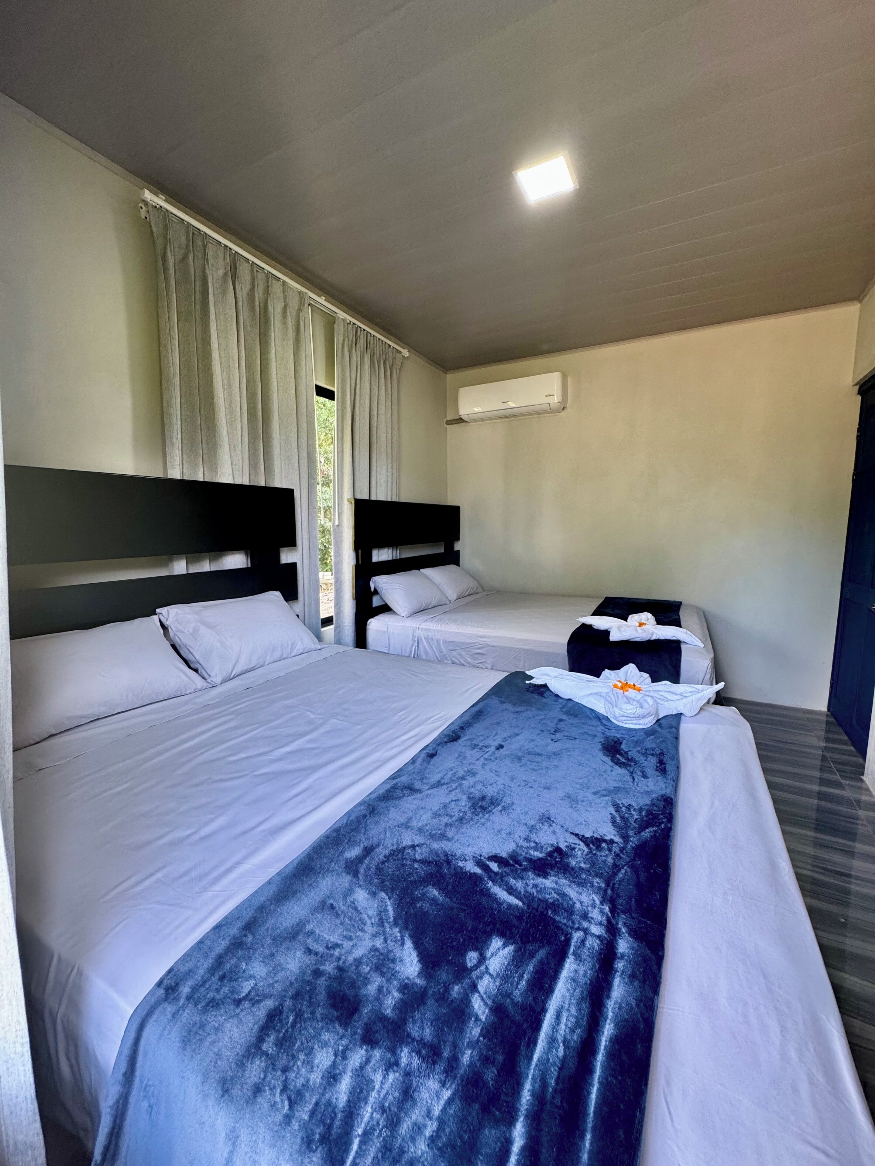 Ein Hotelzimmer mit zwei Betten, einem Vorhangfenster, einer Klimaanlage und einer Tür.