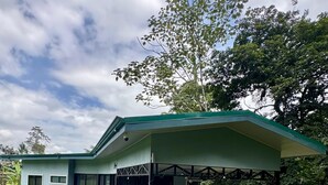 A modern house with a covered patio area, a lawn, and various plants. - Hidden River Lodge (La Fortuna)