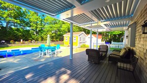 Un patio extérieur couvert avec une piscine, du mobilier d’extérieur et une vue sur une maison en arrière-plan.