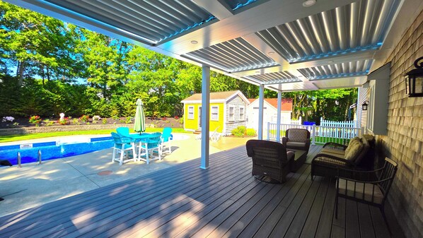 A covered outdoor patio with a pool, outdoor furniture, and a view of a house in the background.