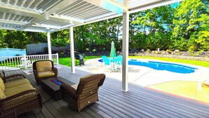 Une terrasse extérieure couverte, aménagée avec des meubles en osier, une piscine et un jardin.