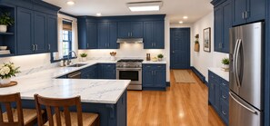 A kitchen with dark blue cabinets, a marble countertop, stainless steel appliances, and wooden flooring.