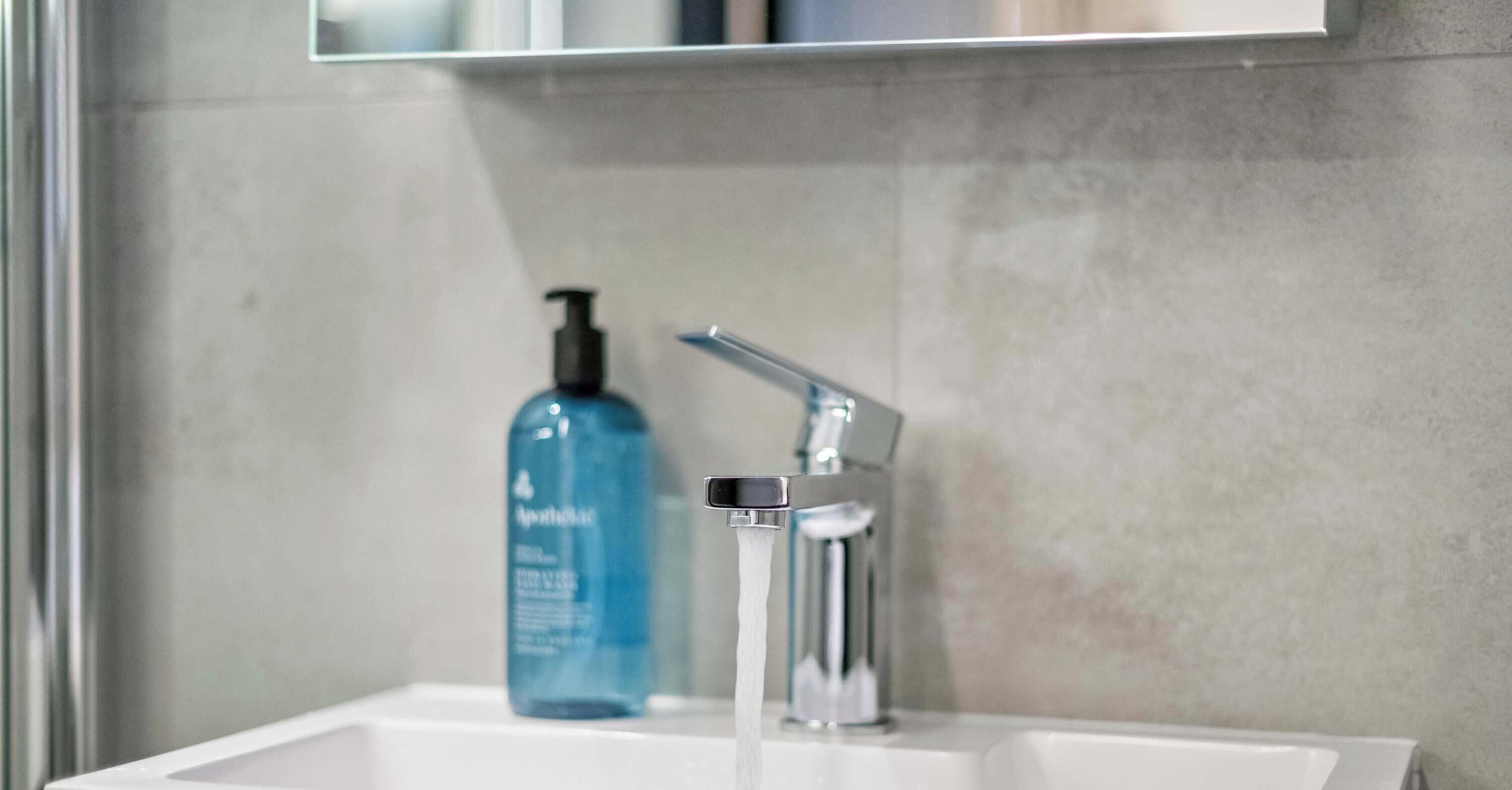 Un baño con un lavabo blanco, un grifo cromado y una botella azul de jabón líquido.