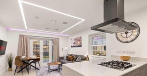 A modern kitchen with a gas stove, a dining area with a table and chairs, a sofa, and a large window. - Fatherson Road, Reading (Berkshire)