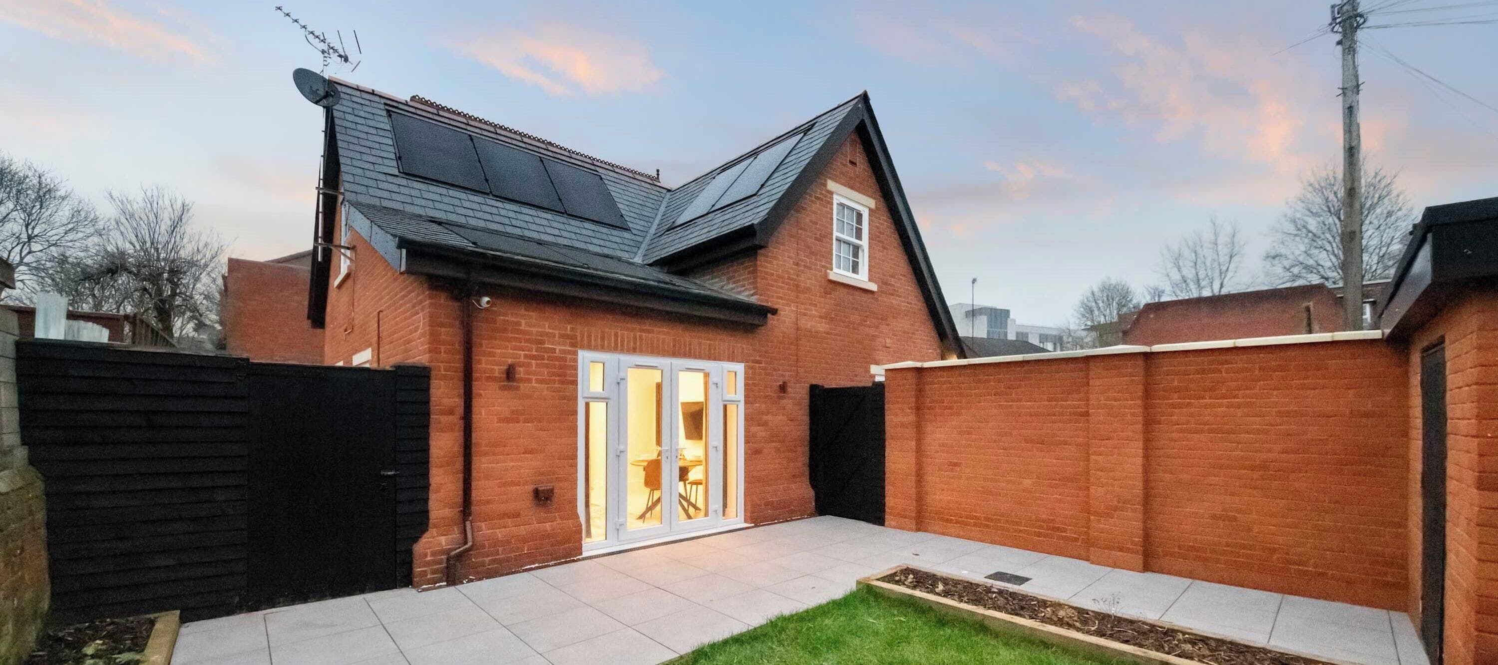 A brick house with a tiled patio, a sliding glass door, and a black fence.