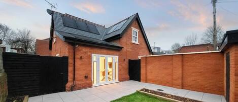 A brick house with a tiled patio, a sliding glass door, and a black fence.