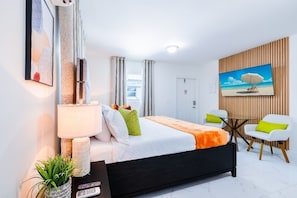 A modern hotel room with a bed, a desk, a chair, a TV, and a painting on the wall.