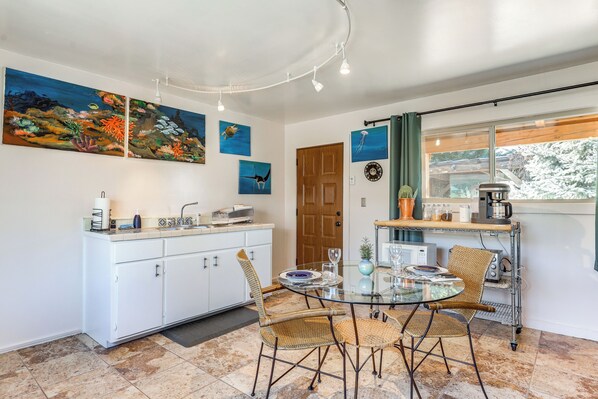 Una cucina moderna con mobili bianchi, un tavolo da pranzo in vetro, sedie in vimini e una macchina per caffè.