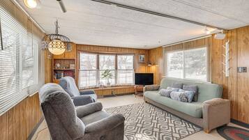 A cozy living room with a sofa, armchairs, a TV, and a patterned rug.