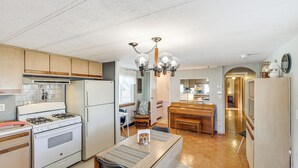 Een keuken met een kookplaat, koelkast, houten kasten, een eettafel met stoelen en een kroonluchter.