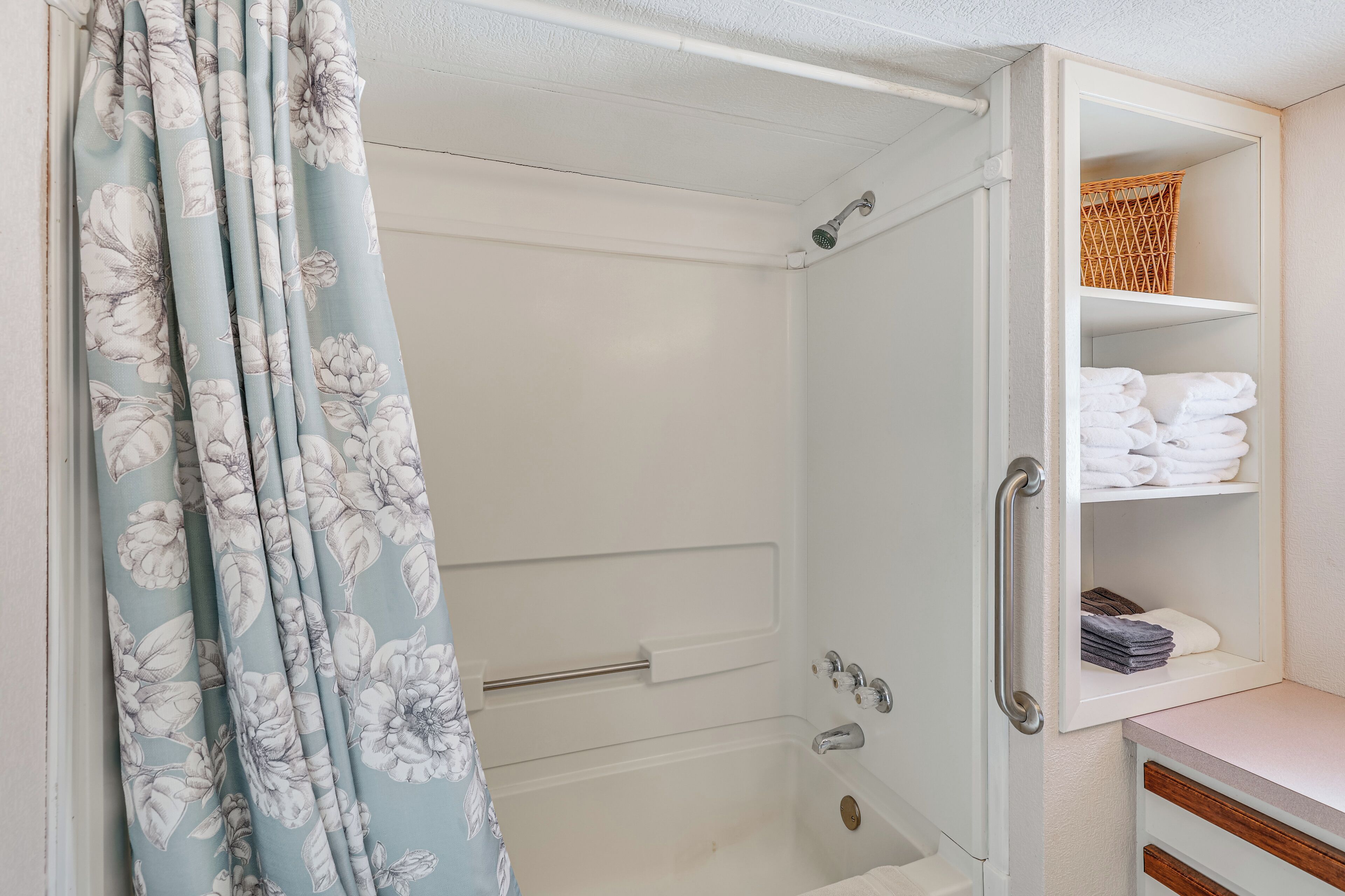 A bathroom with a shower, a towel rack, and a shelf with folded towels.