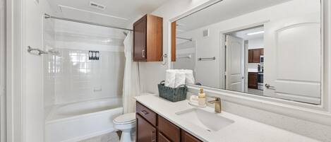Un baño moderno con ducha envuelta en vidrio, inodoro blanco, armarios de madera y un espejo grande.