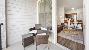A covered patio with wicker furniture and a glass table, leading into a kitchen with wooden cabinets and a refrigerator.