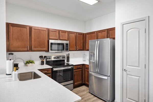 A modern kitchen with wooden cabinets, stainless steel appliances, and a white countertop.