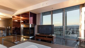 Ein modernes Hotelzimmer mit großem Fernseher, einem Glastisch, einer Couch und einem Balkon mit Blick auf die Stadt.