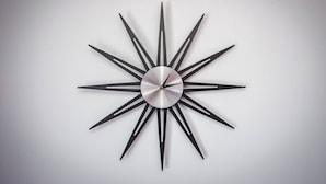 A modern wall clock with a metallic finish and a sunburst design. - Tower Studio – Peaceful Studio with Panoramic View – Next to Cișmigiu Gardens (București)