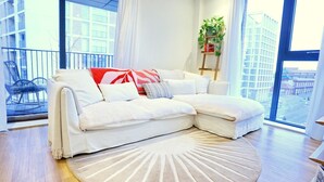 A modern living room with a sectional sofa, a round rug, and large windows offering a city view. - Northern Qtr Corner Flat With Balcony & City Views - Pass the Keys (Manchester)