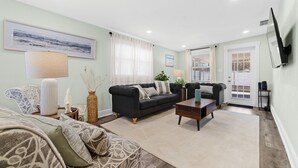 A living room with two sofas, a coffee table, and a TV mounted on the wall. - Near USF, Ybor City, Busch Gardens/RayJ Stadium + TV Backyard  & Games, Slps 8! (Tampa)