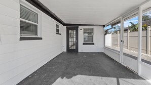 A covered patio area with a black door, white walls, and a concrete floor. - Near USF, Ybor City, Busch Gardens/RayJ Stadium + TV Backyard  & Games, Slps 8! (Tampa)