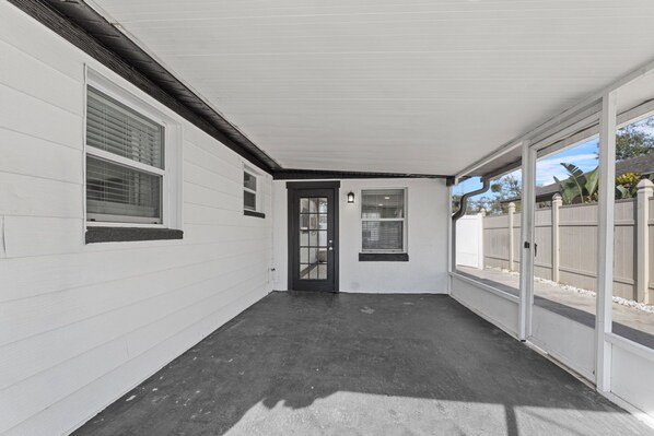 A covered patio area with a black door, white walls, and a concrete floor.