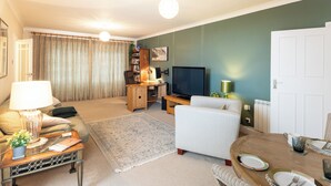 Sala de estar com sofá, mesa de centro, televisão e mesa de jantar posta para dois.