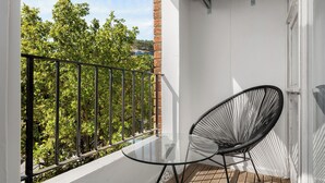 A balcony with a glass table and a black chair, overlooking a lush green area. - Vibrant Cascades Studio | Balcony | WiFi (Cape Town)