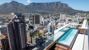 A high-rise building with a rooftop pool and a view of a cityscape and mountains in the background. - Highest Penthouse in City - Pool and Panoramic Views (Cape Town)