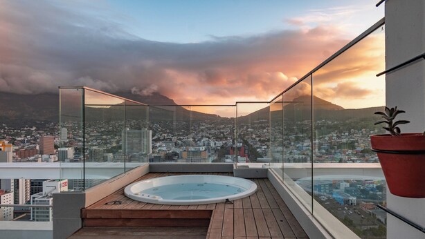 A rooftop terrace with a hot tub, glass railings, and a city view. - Highest Penthouse in City - Pool and Panoramic Views (Cape Town)