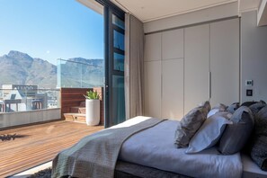 A modern bedroom with a large bed, a balcony with a view of mountains, and a cityscape. - Highest Penthouse in City - Pool and Panoramic Views (Cape Town)