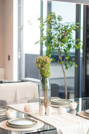 A dining table with plates, a vase with flowers, and a glass partition. - Highest Penthouse in City - Pool and Panoramic Views (Cape Town)