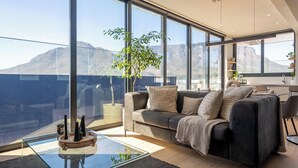 A modern living room with a large window, a sofa, a coffee table, and a plant. - Highest Penthouse in City - Pool and Panoramic Views (Cape Town)