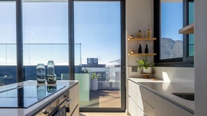 A modern kitchen with large windows, a view of mountains, and a balcony with plants. - Highest Penthouse in City - Pool and Panoramic Views (Cape Town)