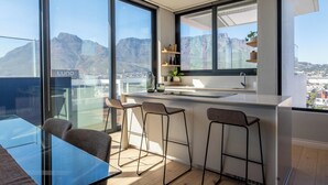 A modern kitchen with large windows, a bar area, and a view of mountains. - Highest Penthouse in City - Pool and Panoramic Views (Cape Town)