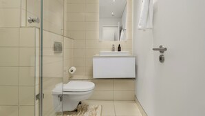 Une salle de bain moderne avec une douche à parois de verre, des toilettes, un lavabo avec un miroir au-dessus et une serviette accrochée au mur.
