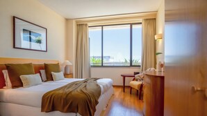 Habitación de hotel con una cama grande, un escritorio, una silla, una lámpara y vistas a zonas verdes.