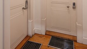 Deux portes blanches, marquées A et B, avec une grille de ventilation en métal au sol, entre les deux.