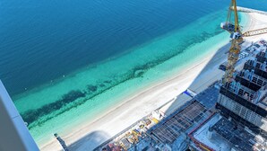 Vista aérea de una zona costera con mar azul transparente, una playa de arena y una obra en construcción con una grúa.