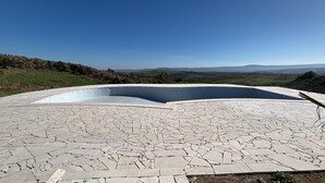 A swimming pool with a unique mosaic tile design, surrounded by a landscape with distant hills.