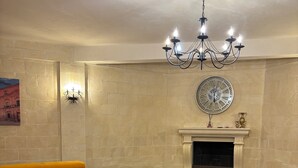 A living room with a large yellow sectional sofa, a fireplace, a round clock, and a chandelier.