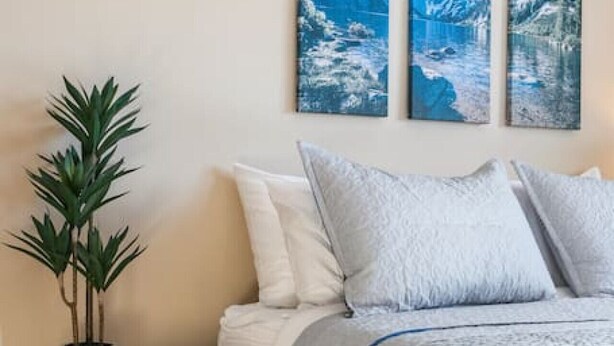 A bedroom with a bed, a bedside table with a plant, and three wall-mounted paintings. - Fireplace! Fully Fenced Yard! (Green Bay)