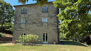 Un bâtiment en pierre doté de deux balcons, d’un petit jardin et d’une porte.